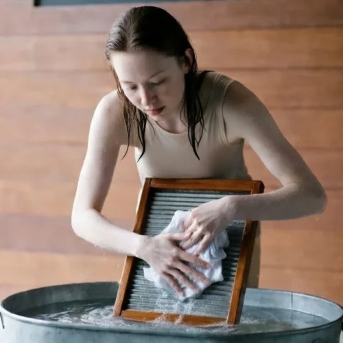 Woman hand-washing clothes with washboard.